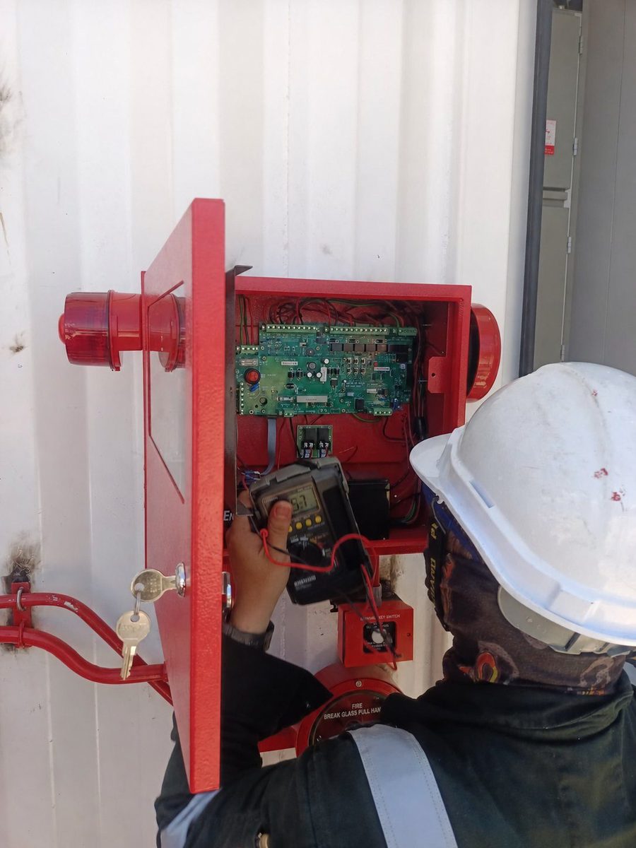 Technician inspecting an open fire suppression control panel with a test meter